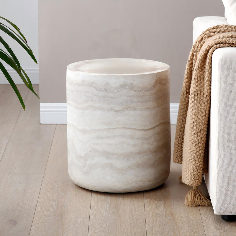 Beige round travertine side table next to a white sofa with a cozy blanket in a living room.