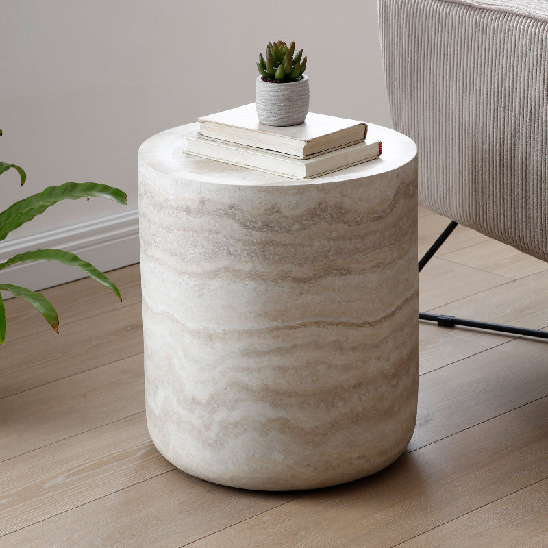 Modern round travertine stone side table with books and a plant beside a grey sofa.
